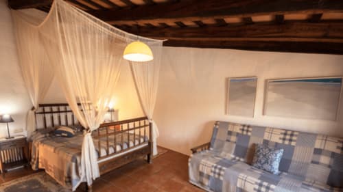 Dormitorio rústico en el B&B Can Gat Vell de Girona con cama con dosel, vigas de madera y acogedor rincón de estar