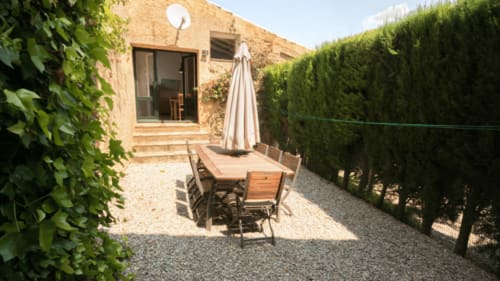 Patio rústico en el alojamiento Can Gat Vell B&B de Girona con mesa de comedor, sombrilla y setos frondosos