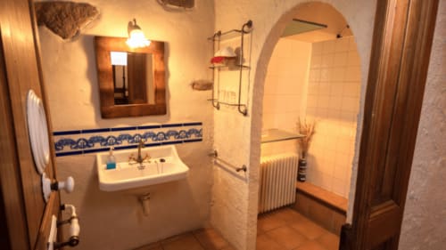 Baño rústico en Can Gat Vell B&B en Girona con ribete de azulejo azul tradicional, lavabo mural y ducha abovedada