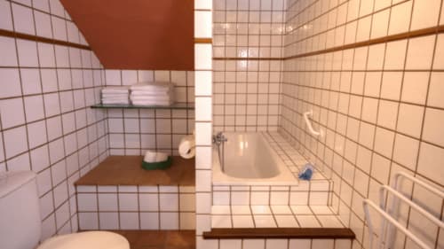 Baño compacto en la casa rural Can Gat Vell en Girona con azulejos blancos, bañera, inodoro y almacenamiento de madera.