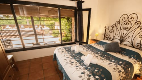 Habitación luminosa en Can Gat Vell B&B en Girona con cabecero ornamentado, ropa de cama estampada y vista al Empordà desde el balcón