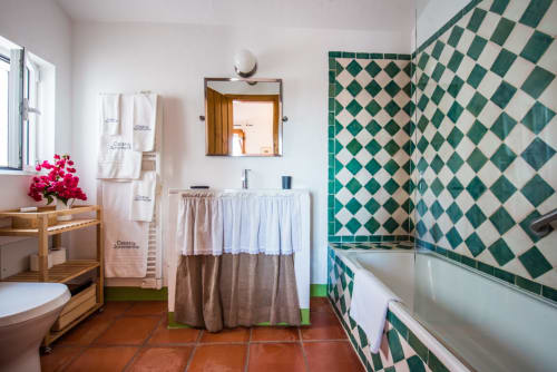Banheiro espaçoso na villa Casas de Juromenha com azulejos verdes e brancos em padrão de diamante, bancada de madeira e piso de terracota