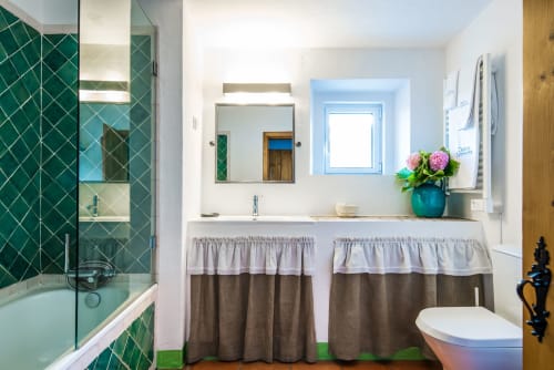 Banheiro moderno na villa Casas de Juromenha com chuveiro de azulejo verde, pia dupla e janela iluminada