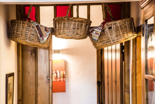 Cestos rústicos tecidos pendem acima de portas de madeira na villa Casas de Juromenha, apresentando vidros vermelhos e calor natural
