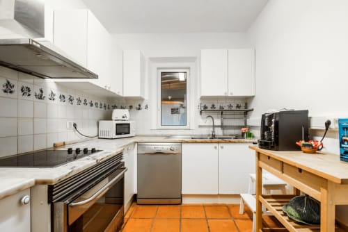 Cozinha moderna branca com piso de azulejos laranja, eletrodomésticos em aço inoxidável e bancadas de madeira na villa Casas de Juromenha