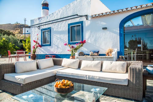 Terraço de villa à beira-mar em Casas de Juromenha com assentos em vime, almofadas brancas e vista para o farol em Portugal