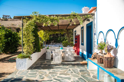 Terraço da villa Casas de Juromenha com pérgola coberta de hera, mesa de jantar, portas azuis e pátio de pedra em Juromenha, Portugal