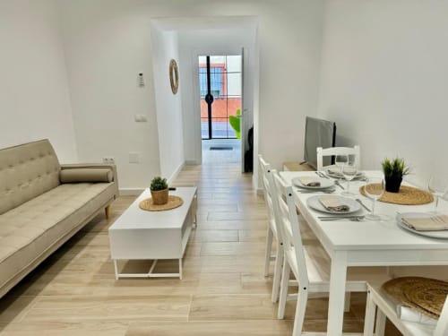 Sala de estar moderna en apartamento de Nerja con zona de comedor, sofá beis, mesa blanca y puertas de cristal hacia balcón