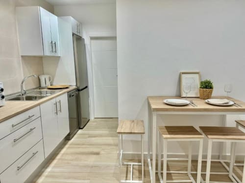 Cocina y comedor modernos en apartamento de Nerja Holiday Homes con muebles blancos, electrodomésticos de acero inoxidable y madera