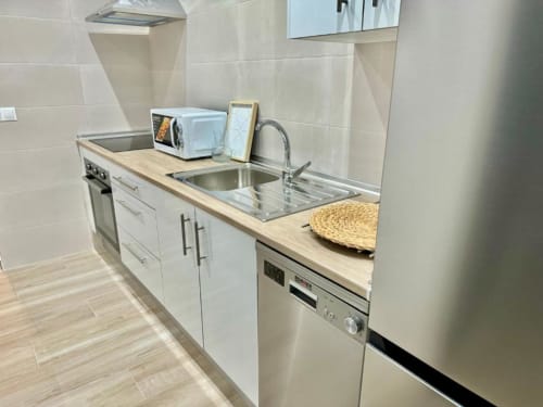 Cocina moderna en apartamento de Nerja Holiday Homes con armarios blancos, fregadero de acero inoxidable, microondas y azulejos beige