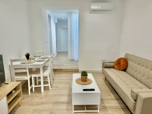 Moderno apartamento en Nerja con salón de sofá beis, mesa comedor blanca, suelos de madera y decoración contemporánea