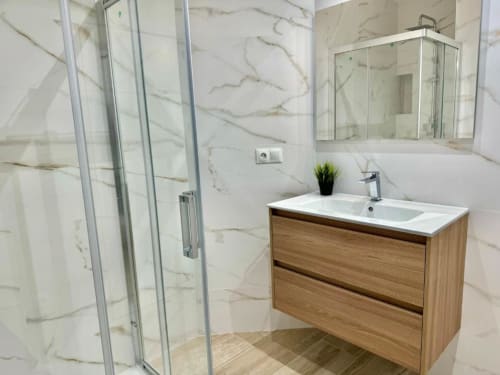 Baño moderno en apartamento de Nerja Holiday Homes con paredes de mármol, tocador de madera, lavabo blanco y ducha con mampara de vidrio