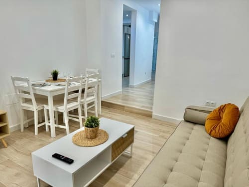 Moderno salón de apartamento en Nerja con zona de comedor, sofá beige, mesa blanca y suelo de madera