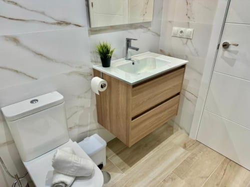 Baño moderno en apartamento Nerja Holiday Homes con baldosas de mármol, mueble de madera, inodoro blanco y planta decorativa