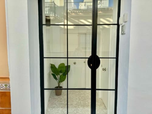Entrada de puerta de cristal con marco negro al apartamento Nerja Holiday Homes con maceta visible en el interior