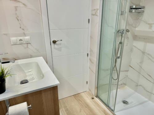 Baño moderno en apartamento Nerja Holiday Homes con azulejos de mármol, lavabo blanco, mampara de ducha de cristal y suelo de madera