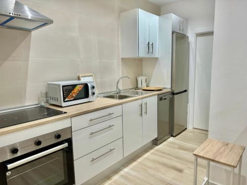 Cocina moderna en apartamento de Nerja Holiday Homes con muebles blancos, electrodomésticos de acero inoxidable y efecto madera