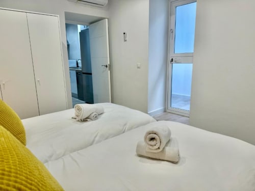Dormitorio de apartamento en Nerja Holiday Homes moderno con ropa de cama blanca, toallas enrolladas y acceso a balcón por puerta de cristal