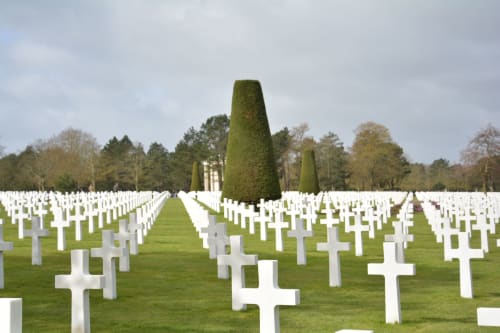 Croix blanches du cimetière américain de Normandie près de Bayeux, avec cyprès et pelouses verdoyantes sous un ciel nuageux