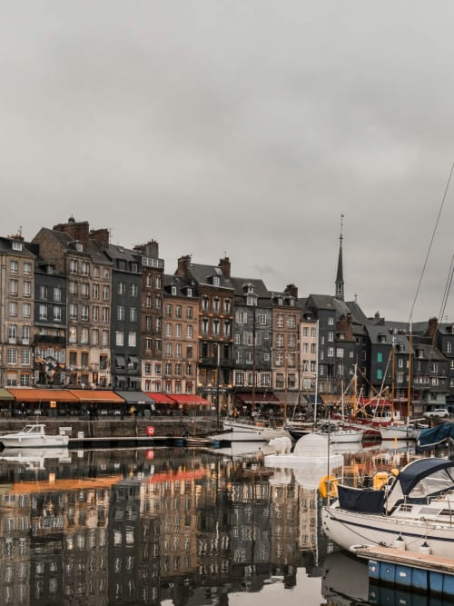 Port pittoresque de Bayeux avec bâtiments historiques, voiliers et reflets sur l'eau près du restaurant Le 58