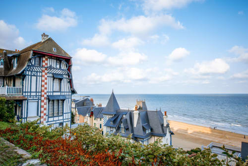L'hôtel Le 58 Bayeux surplombant la plage de sable avec un ciel bleu et l'architecture médiévale en Normandie