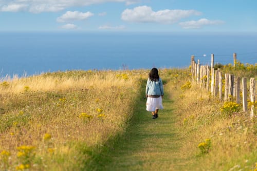 Femme marchant dans un champ doré avec vue sur la mer près de Bayeux, paysage normand