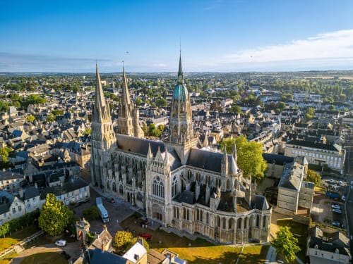 Vue aérienne de la Cathédrale de Bayeux entourée de bâtiments médiévaux et de la rivière, mettant en avant le patrimoine historique normand du Le 58 Bayeux