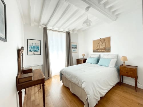 Chambre lumineuse au Le 58 Bayeux avec lit queen-size, tables de nuit en bois, poutres apparentes et décoration nautique.