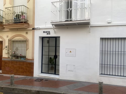 Entrada del apartamento Nerja Holiday Homes en Nueva 29B, fachada blanca con puerta de marco negro y ventanas con rejas