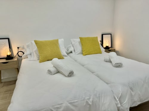 Dormitorio moderno en Nerja Holiday Homes con dos camas, sábanas blancas, almohadas verde lima y lámparas de noche en Nerja, España
