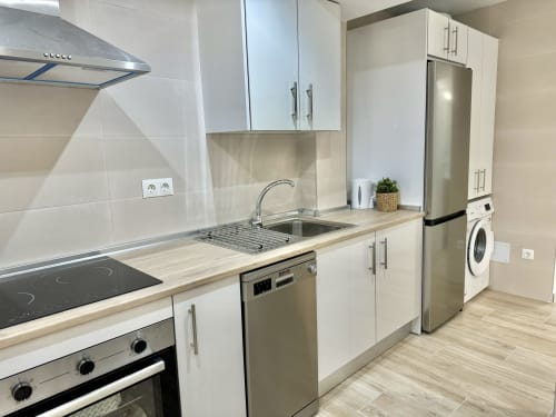 Cocina moderna en apartamento de Nerja Holiday Homes con muebles blancos, electrodomésticos de acero inoxidable y piso de madera clara
