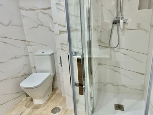 Baño moderno en apartamento Nerja Holiday Homes con azulejos de mármol, inodoro blanco, cabina de ducha cristal y acabados efecto madera