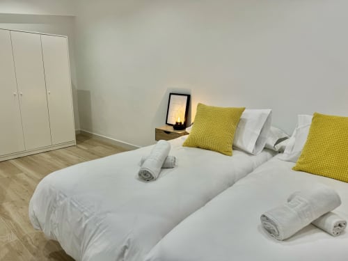Dormitorio moderno en Nerja Holiday Homes con camas gemelas, cojines amarillos, armarios blancos y piso de madera
