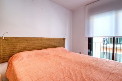 Dormitorio con cabecero tejido, ropa de cama naranja y vistas al balcón en Finques Garcia Enrich, Palafrugell