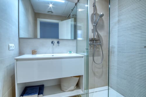 Baño moderno del hotel Finques Garcia Enrich en Palafrugell con tocador blanco, espejo y ducha abierta