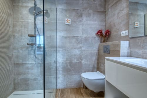 Baño moderno en el hotel Finques Garcia Enrich en Palafrugell con ducha a ras de suelo, tocador blanco y flores rojas
