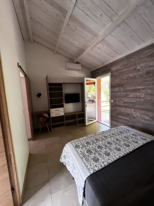 Chambre de mini villa au Maquis Plage avec lit, mur en bois, espace bureau et accès à la terrasse