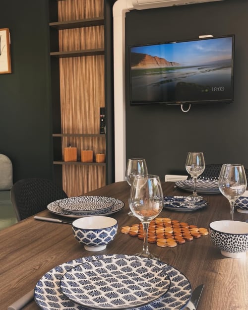Salle à manger de la villa Le Maquis Plage avec table dressée, vaisselle à motifs, verres à vin et vue sur plage à la télévision