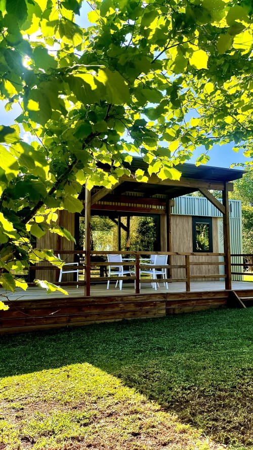 Terrasse de villa moderne en bois à Le Maquis Plage avec chaises blanches, gazon verdoyant et tonnelle de vignes à Poggio-Mezzana