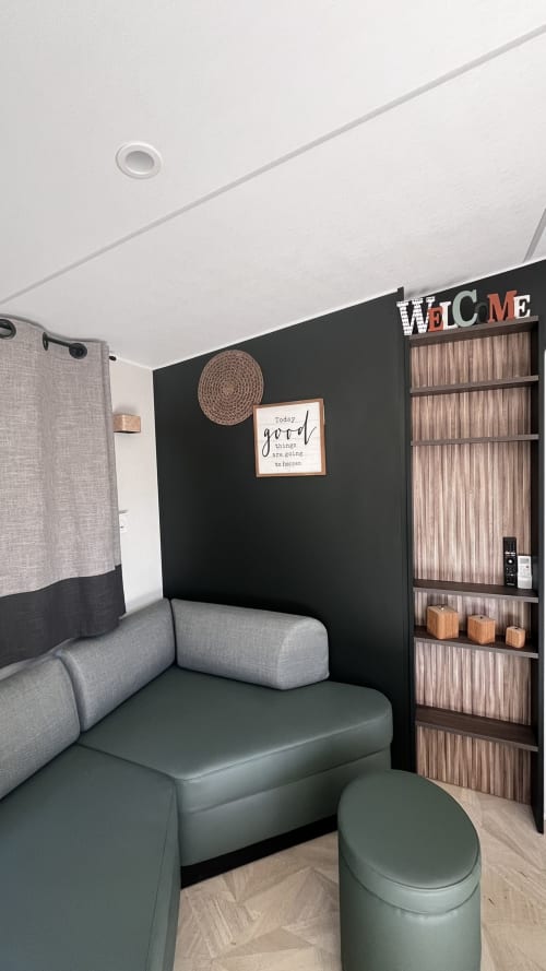 Salon de mobil-home moderne avec mur noir, sièges gris, étagères bois et panneau d'accueil au Maquis Plage