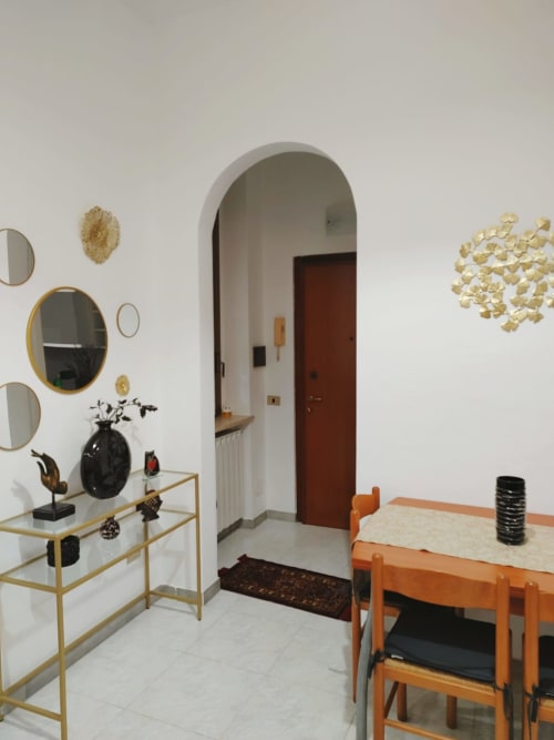 Ingresso dell'Apartment Mazzini della Collezione V a Turate, Italia, con arredamento moderno, accenti dorati e sala da pranzo arancione