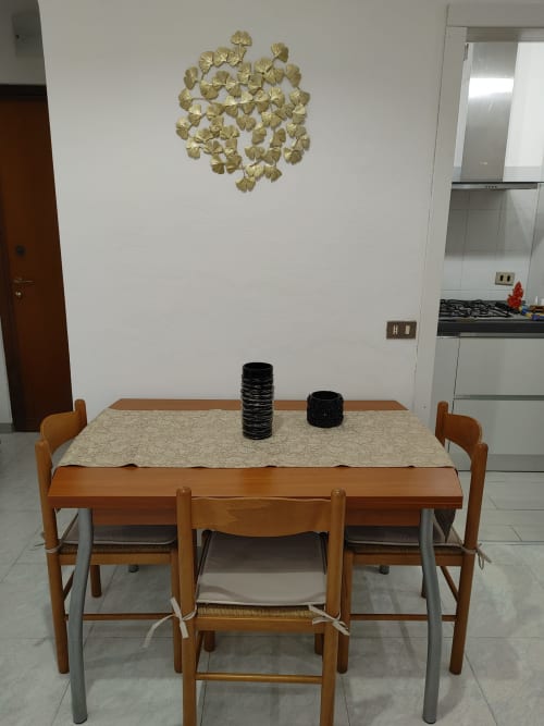 Zona pranzo moderna dell'Appartamento Mazzini con tavolo in legno, sedie, runner beige e arte murale in foglia d'oro presso l'hotel Turate