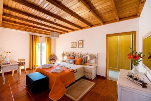 Bright bedroom at Home Alliance B&B in Bombarral with wooden beams, orange accents, and modern amenities