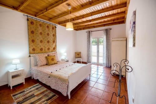 Spacious double bedroom with wooden beams, white bed, terracotta tiles, and patio access at Home Alliance B&B in Bombarral