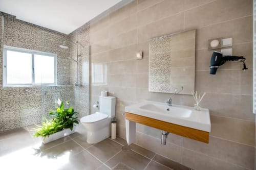 Banheiro moderno da Suíte Quarto Duplo Superior Home Alliance com azulejos em mosaico, pia branca, vaso sanitário, espelho e janela