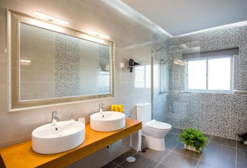 Banheiro moderno da Home Alliance Bombarral com dupla pia, espelho iluminado, chuveiro walk-in e detalhes em azulejos mosaicos