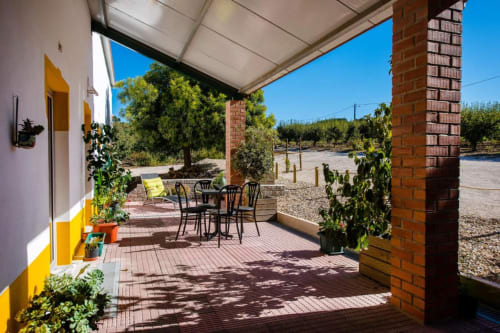 Covered patio with dining table and lounge chair at Home Alliance B&B in Bombarral, Óbidos, Portugal. Brick columns, potted