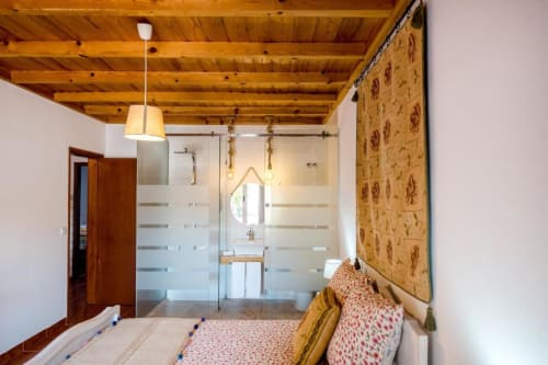 Quarto moderno com vigas de madeira no teto, chuveiro de vidro, papel de parede estampado e cama confortável na Home Alliance