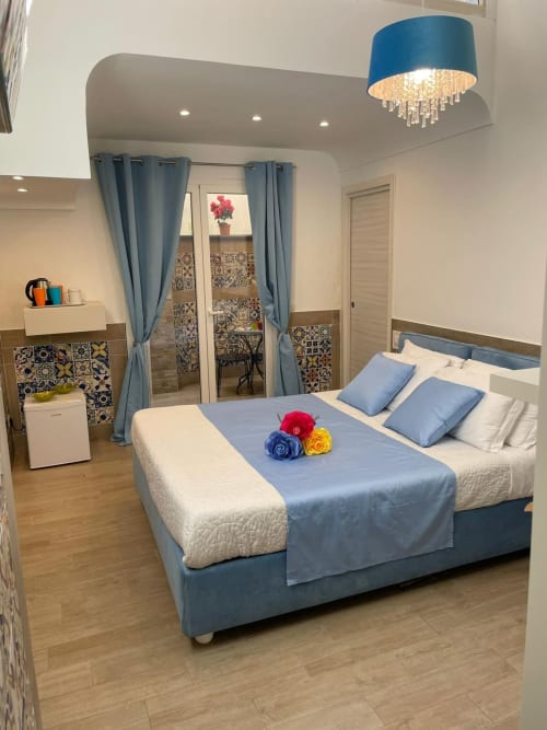 Camera moderna presso San Nicola Suite Mini Apartments a Sorrento con letto imbottito blu, fiori decorativi e specchi