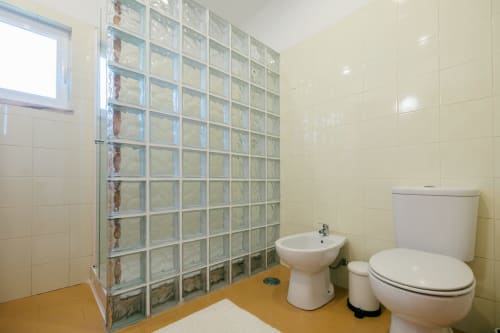 Modern bathroom at Figueira House villa with glass block shower, toilet, bidet, and yellow floor in Sesimbra